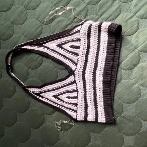 Stickad randig crop top i svart och vitt - Säljer en stickad crop top med svartvita ränder och coolt geometriskt mönster. Toppen har breda axelband och är ärmlös, perfekt för att styla med höga jeans eller kjol. Mjuk och stretchig, passar dig som gillar unika plagg med retrovibbar.