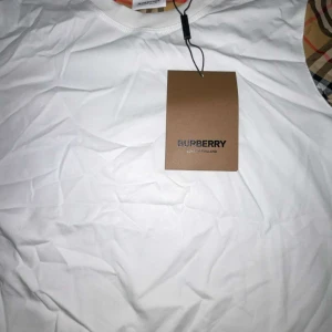 Vit linnetopp från Burberry strl S - Snygg vit linnetopp från Burberry med klassiska rutiga detaljer vid ärmöppningarna. Toppen har rund halsringning och ärmlös design, perfekt för en clean och stilren look. Ikonisk Burberry-tag medföljer. Passar dig som gillar exklusiva och tidlösa plagg.