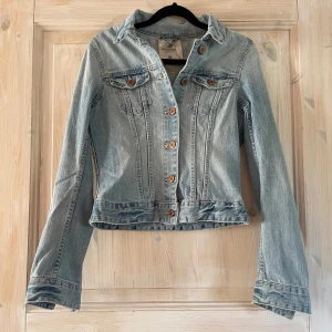 Ljusblå jeansjacka från H&M - Snygg ljusblå jeansjacka från H&M med klassisk krage, bröstfickor med lock och knappar framtill. Jackan har figurnära passform och långa ärmar. Inga defekter, nypris 500kr