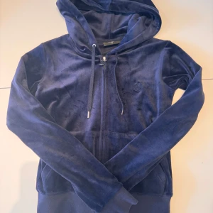Juicy couture zip up hoodie mörkblå - En mörkblå zip up hoodie på Juicy Couture i storlek XS. Materialet är mjukt och perfect för chill dagar. Som man kan se bilden så har ena toppen av snöret till huvan åkt av men det märks knappt när man har på den. Pris för en ny är 1300kr på deras webbsida.