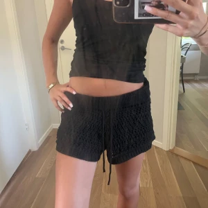 Svarta stickade shorts med snörning - Svarta stickade shorts med snyggt virkat mönster och bred resår i midjan. De har snörning framtill för extra passform och är perfekta för en chill och avslappnad look. Mjuka och bekväma, passar perfekt till sommaren.