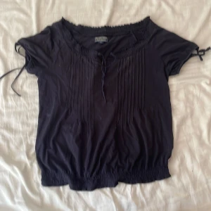 Marinblå blus från Ralph lauren  - Marinblå blus från Polo Jeans Company by Ralph Lauren med korta ärmar och knytband vid ärmslut och halsringning. Smockad nederkant och fina veck framtill ger en avslappnad men ändå söt look. 