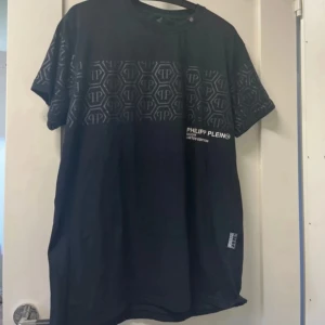 Svart Philipp Plein t-shirt med mönster - Svart t-shirt från Philipp Plein med korta ärmar och coolt hexagonmönster med PP-logga över bröstet och ärmarna. Limited Edition-tryck på framsidan och en snygg metallpatch med logga i nacken.