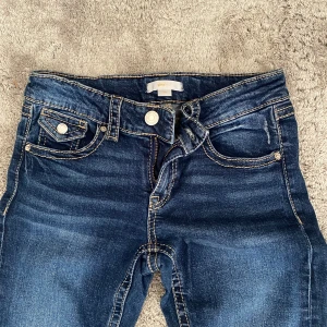 Mörkblå jeans från Gina Tricot, strl 164 - Snygga mörkblå jeans från Gina Tricot i storlek 164. Klassisk femficksmodell med kontrastsömmar och raka ben. Jeansen har coola detaljer på bakfickorna och stängs med dragkedja och knapp. Perfekta till en avslappnad streetstil. Lågmidjade och passar även xs-s. 