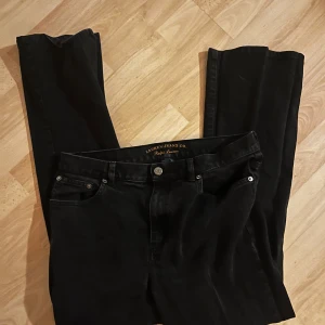 Svarta jeans från Ralph Lauren - Snygga svarta jeans från Ralph Lauren Jeans Co. Klassisk femficksmodell med raka ben och silverfärgade detaljer. Jeansen har en stilren look och passar perfekt till en streetinspirerad outfit. Materialet är robust denim i bomull.