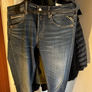 Replay jeans Grover  - Säljer ett par snygga blå jeans från Replay med klassisk femficksdesign och tydliga slitningar framtill. Jeansen har raka ben, normal passform och detaljerade sömmar på bakfickorna. Märkespatch i läder baktill och Replay-logga på fickan framtill. 