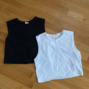 Svart och vit croppad linnetopp Stories S - Två croppade linnetoppar från Stories i storlek S, en i svart och en i vit. Båda är ärmlösa med rund hals. Materialet är mjuk bomull som känns skönt mot huden. Du står för frakten, vid mer info skriv