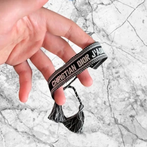 Christian Dior svart tygarmband - Svart och vitt tygarmband från Christian Dior med texten 'CHRISTIAN DIOR J'ADIOR' broderad runt om. Armbandet har en enkel och stilren design med knytning för justerbar passform. Perfekt accessoar för att lyfta din outfit med en lyxig touch. Ny pris 2000kr.