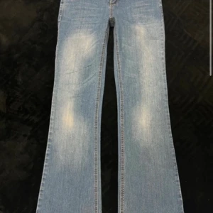 Ljusblå bootcut jeans med slitningar - Säljer ett par ljusblå bootcut jeans med snygga slitningar på låren. Jeansen har klassisk femficksdesign, dragkedja och knapp framtill. Materialet är jeans i bomull och passformen är loose med breda ben. Perfekta för dig som gillar retrovibbar och avslappnad stil.