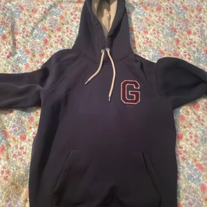 Mörkblå hoodie från GANT med G-logga - Säljer en mörkblå hoodie från GANT i storlek S. Den är väldigt sällan använd och skicket är åtminstone 9/10 med inga defekter.