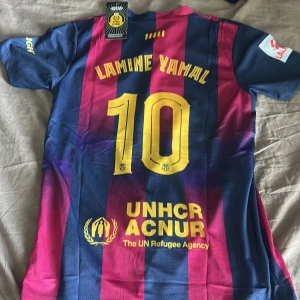 FC Barcelona Lamine Yamal #10 tröja - Säljer en officiell FC Barcelona matchtröja med Lamine Yamal och nummer 10 på ryggen. Tröjan är kortärmad, har breda blå och röda ränder, gula detaljer och sponsorer som Spotify, UNHCR och Ambilight. La Liga-märke på ärmen. Tillverkad i lätt och ventilerande polyester.