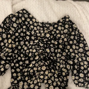 Svart blommig topp från Paulmarc - Supersöt svart topp från Paulmarc i storlek S med vita och gula blommor över hela tyget. Klänningen har lång ärm och snygg rynkning framtill som ger en cool detalj. Perfekt för dig som gillar blommigt och vill sticka ut lite extra.