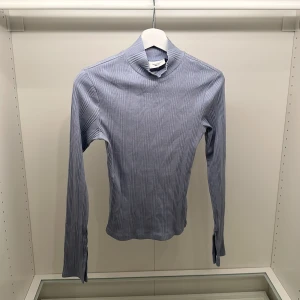 Blå ribbad polotröja Gina Tricot - Snygg ljusblå ribbad polotröja från Gina Tricot, modell Basically Basics. Tröjan har lång ärm men en slits längst ner vid armen, smal passform och hög krage. Materialet är mjukt och stretchigt. Diskret slits vid ärmslut för extra detalj. Enkel att styla till jeans eller kjol.