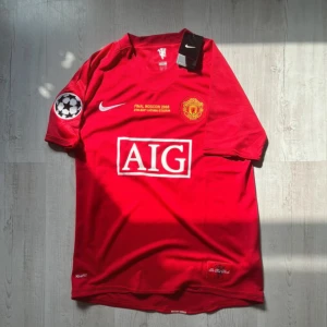 Manchester United Ronaldo 7 Finaltröja - Manchester Uniteds officiella finaltröja från Champions League-finalen i Moskva 2008. Röd med gula och vita detaljer, AIG-logga på bröstet, klubbmärke och Nike Swoosh. Nummer 7 och Ronaldo på ryggen. Kortärmad modell i lätt funktionsmaterial.