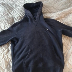 Mörkblå hoodie från Polo Ralph Lauren - Snygg mörkblå hoodie från Polo Ralph Lauren med klassisk huva och känguruficka. Tröjan har det ikoniska lilla broderade logot på bröstet och är tillverkad i mjuk bomull. Perfekt för en chill och stilren look.