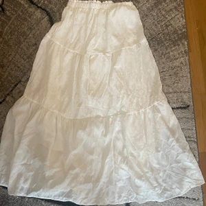 Vit långkjol med volanger - Säljer en vit långkjol med volanger och resår i midjan. Kjolen har en luftig och flowy känsla, perfekt för varma dagar. Materialet är lätt och har en subtil struktur som ger extra liv till plagget. Enkel att matcha med både toppar och sneakers. Strl s. Från SHEIN. Har använt 1 gång. Pris går att diskutera 