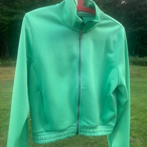 Grön fin tröja från SOC, storlek M - Snygg grön tröja från SOC i storlek M. Jackan har dragkedja framtill, hög krage och två fickor med dragkedja. Perfekt för utomhusaktiviteter och träning. Elastisk nederkant ger en skön passform och sportig look.