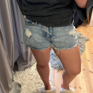 Blå jeansshorts med slitningar - Säljer ett par ljusblå jeansshorts med råa, fransiga kanter och slitna detaljer både fram och bak. Klassisk femficksmodell.💗