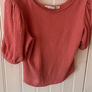 Rosa blus  -  Rosa blus från 157 med korta puffärmar. Köpt för kanske 2 år sedan men har i princip bara hängt i garderoben. Storlek L men upplevde den mer som M eftersom den är ganska kort 