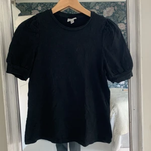 Svart topp med puffärm från Vero Moda - Svart topp från Aware by Vero Moda med puffiga korta ärmar och rund halsringning. Enkel och stilren design i mjuk bomull, perfekt att matcha med jeans eller kjol. Snygg passform och klassisk look.