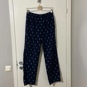 Ralph Lauren pyjamasbyxor  - Mörkblå pyjamasbyxor från Ralph Lauren – lyxig komfort för både kväll och helg. Tillverkade i mjukt bomullstyg med avslappnad passform och många Ralph Lauren-loggor. Perfekta för mysiga hemmakvällar eller som stilren loungewear. Inga defekter – rena, fräscha och redo att användas!
