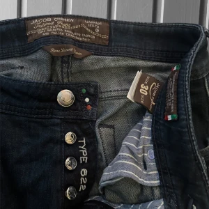 Jacob Cohen  type 622  - Snygga mörkblå jeans från Jacob Cohen, modell type 622. Klassisk femficksdesign med exklusiva detaljer som broderad logga och unika knappar. Jeansen har rak passform och är tillverkade i mjukt denimtyg med italienskt hantverk. Perfekta för dig som gillar stilrena och lyxiga jeans. Öppnade längst ner (köpta så).