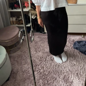 Svart långkjol med rynkade detaljer från Gina Tricot  - Säljer en svart långkjol med snygga rynkade detaljer längs sidorna från Gina Tricot . Kjolen har en tight passform som framhäver figuren och är gjord i ett mjukt, stretchigt material. Perfekt för dig som gillar minimalistisk stil med en twist. Skriv för fler bilder eller frågor!