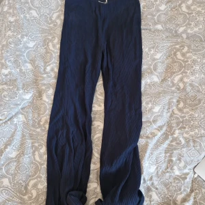 Mörkblå vida byxor från NA-KD - Säljer ett par mörkblå vida byxor från NA-KD i storlek 36. Byxorna har en ribbad struktur, hög midja och är tillverkade i ett mjukt, flowy material. Perfekta för en chill och trendig look. Färgen är dark navy och modellen heter Flounce Hem Pants.
