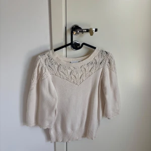 Beige stickad topp med spetsdetaljer - Supersöt beige stickad topp från Saint med korta puffärmar och vackra spetsdetaljer upptill. Rund halsringning och ribbade muddar ger en chill men ändå fin vibe. Perfekt för dig som gillar kläder med fina detaljer och som också funkar till vardagen.