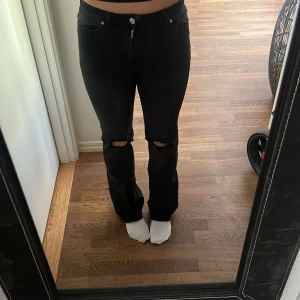 Svarta bootcut jeans från ONLY - Svarta jeans från ONLY med bootcut passform och hål vid knäna för en edgy vibe. Klassisk femficksmodell med dragkedja och knapp framtill. Jeansen är i stretchigt bomullsmaterial och har hög midja som sitter snyggt.