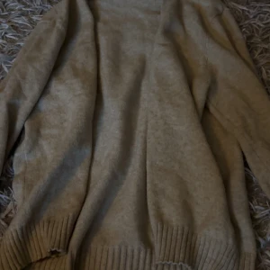 Beige stickad kofta från VILA - Mysig beige stickad kofta från VILA i storlek S. Koftan har långärmad design och bred ribbad mudd vid ärmslut och nederkant. Perfekt för lager-på-lager och chill höst- och vinterstil.