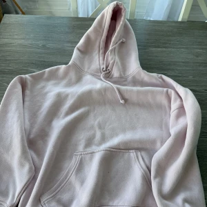 Ljusrosa hoodie med huva och ficka - Mysig ljusrosa hoodie med stor huva och dragsko. Tröjan har en klassisk känguruficka framtill och är tillverkad i mjukt material, perfekt för chill dagar. Långärmad och loose fit för en avslappnad stil.