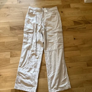 Beiga cargopants, strl 40 - Snygga beiga cargopants med raka ben och stora fickor på sidorna. Byxorna är tillverkade i bomull och har en avslappnad passform. Perfekta för en chill och trendig look.