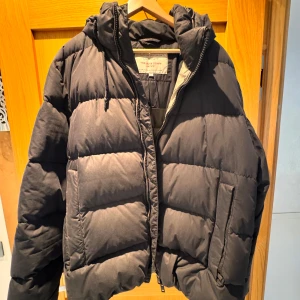 Svart pufferjacka GANT XL - Säljer en svart pufferjacka från GANT, modell The Alta Down Jacket. Jackan har huva med snörning, dragkedja framtill och två stora fickor. Perfekt för kalla dagar med sin dunfyllning och klassiska look. Passar dig som gillar stilren och sportig vibe. Köptes för 3500kr och knappt använd! 