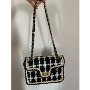 Rutig axelväska - Snygg axelväska i svart och vitt rutigt tyg med flätade kanter och guldfärgad kedja i axelremmen.