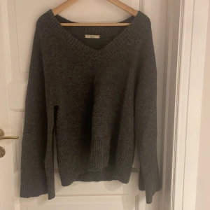 Mörkgrå stickad tröja Gina Tricot - Mysig mörkgrå stickad tröja från Gina Tricot med v-ringad hals och långa ärmar. Tröjan har en loose fit och breda ribbade muddar vid ärmslut och nederkant. Blir inte nopprig, nypris va 699