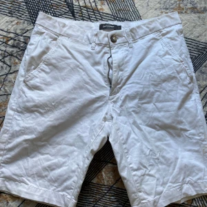 Vita bomullsshorts från Dressmann - Klassiska vita shorts från Dressmann i bomull med normal passform. De har fickor fram och bak, bälteshällor och stängs med knapp och dragkedja. Perfekta för varma dagar och enkel att matcha med allt. Storlek M men passar som S också 