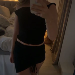 Svart kortkjol med snörning från NA-KD - Supersnygg svart kortkjol från NA-KD med trendig snörning och rynkade detaljer framtill. Perfekt till festligheter! 🤩