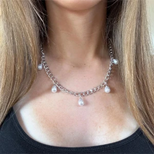 Pärlhalsband Silver - Stilrent halsband med grov silverfärgad kedja och fem droppformade pärlor som hänger längs kedjan. Perfekt för att ge din outfit en cool och trendig touch. Passar dig som gillar statement-smycken och vill sticka ut lite extra. OBS, postat tidigast lör (instabox) eller sön (PostNord)