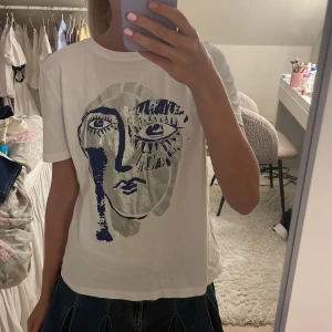 Vit t-shirt med tryck - Vit t-shirt med ett stort, ansiktstryck i blått och grått framtill