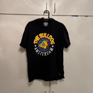 The Bulldog Amsterdam svart t-shirt - Svart t-shirt från The Bulldog Amsterdam med stor färgglad bulldog-logga på bröstet. Klassisk passform och rund hals. Trycket har gula, röda, blå och vita detaljer. Vintage