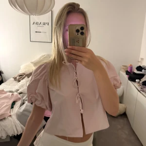 Ljusrosa blus med puffärm från Gina Tricot - Supersöt ljusrosa blus med puffiga korta ärmar och knyt framtill. Köpt från gina och är använd få gånger❤️