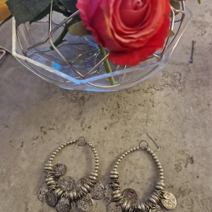 Stora örhängen med mynt i silverfärg - Säljer ett par stora, runda örhängen i silverfärg med pärlformade detaljer och flera hängande mynt. Ger en cool boho-vibe och passar perfekt om du vill sticka ut med accessoarer som syns.