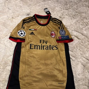 AC Milan Kaka' 22 guld fotbollströja M - AC Milan fotbollströja i guld med svarta och röda detaljer, Adidas-märke och Fly Emirates-tryck. Kaka' 22 på ryggen, Champions League och Respect-patchar på ärmarna. Tillverkad i lätt och ventilerande climacool-material.