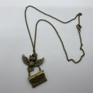 Harry Potter Halsband med uggla och brev  - Unikt halsband i antik bronsfärg med en detaljrik uggla och ett öppningsbart kuvert som hänger under. Kuvertet har graverade blommor och innehåller ett litet brev, inspirerat av Harry Potter. Perfekt för dig som älskar magiska detaljer och snygga accessoarer. Kedjans längd är ca 50cm, uggla ca 3.5x2cm, kuvert ca 2x1.4cm. Materialet är zinc alloy 