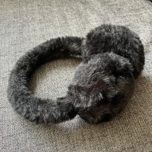 Svarta fluffiga öronmuffar i fuskpäls - Svarta öronmuffar med fluffig fuskpäls.  Bågen är också täckt i samma pälsiga material. Aldrig använda.