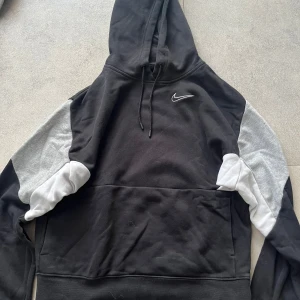 Nike hoodie svart/grå XS - Nike hoodie i svart med grå och vita detaljer på ärmarna. Klassisk huva med snörning och stor ficka framtill. Nike logga broderad på bröstet. 