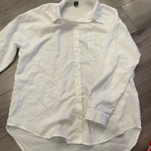 Vit klassisk skjorta med ficka - Vit skjorta från H&M i klassisk modell med lång ärm, bröstficka och knappar hela vägen framtill. Skjortan har en rak passform och är tillverkad i bomull, perfekt till jeans eller kostymbyxor.