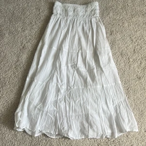 Vit långkjol från Gina Tricot - Luftig och flowy vit långkjol från Gina Tricot med smockad midja och lätt rynkad struktur. Kjolen är tillverkad i mjuk bomull och har en avslappnad passform som ger en chill vibe. Perfekt för varma dagar när du vill känna dig fri och bekväm. Använd mycket men inga märken på det