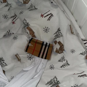 Vit Burberry skjorta med rutiga detaljer - Säljer en snygg vit skjorta från Burberry med klassiska rutiga detaljer i beige, svart och rött längs knappraden och vid manschetterna. Skjortan har broderad logga på bröstet och är långärmad med normal passform. Perfekt för dig som vill sticka ut med stilrena detaljer.